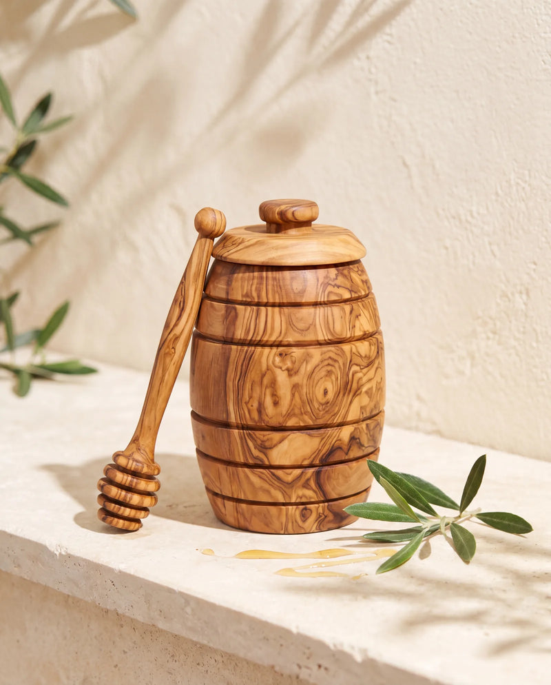 Honigtopf mit Honiglöffel aus Olivenholz auf Steinsims vor mediterraner Putzwand