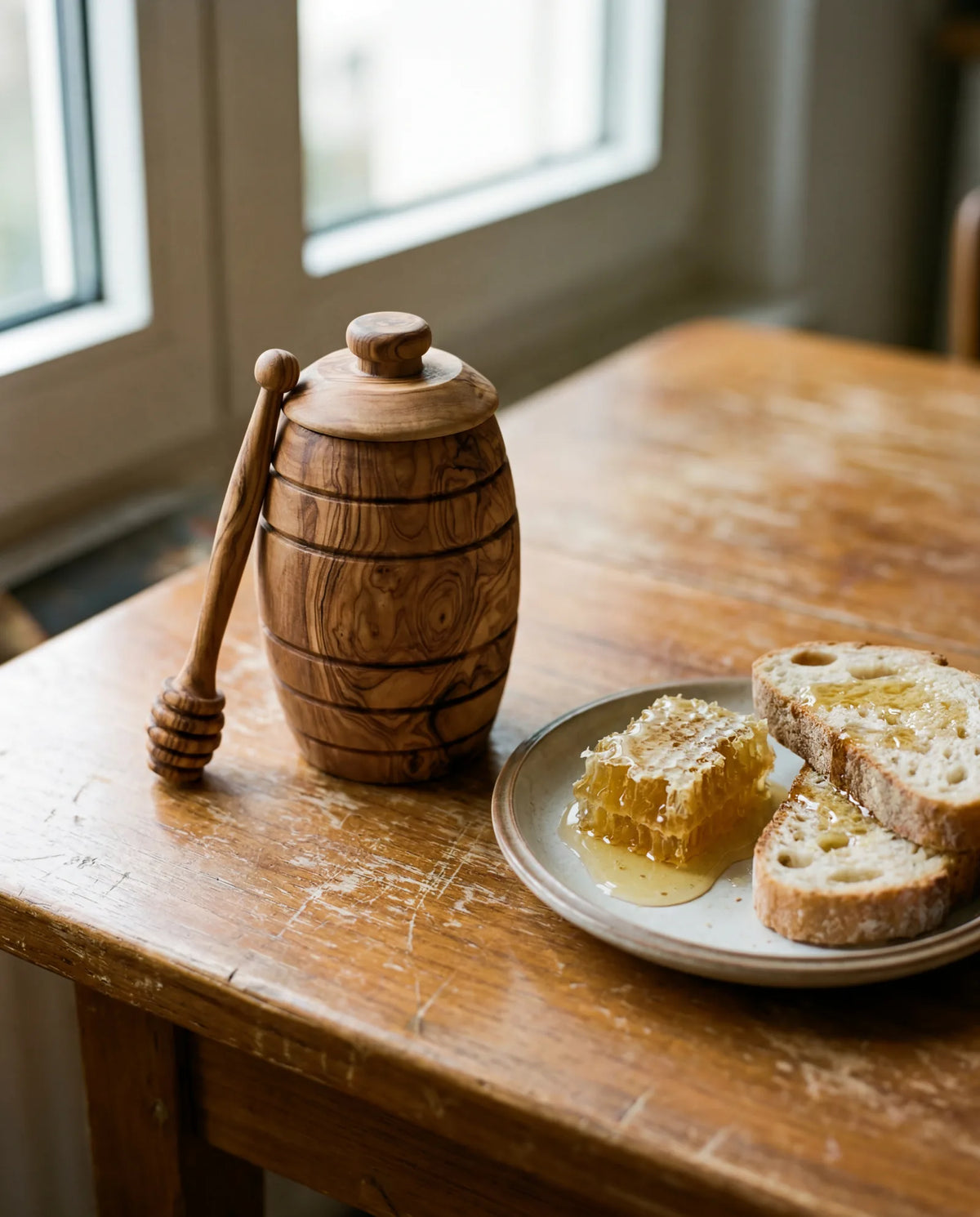 Honigtopf aus Olivenholz mit Honigwabe und rustikalem Brot am Frühstückstisch