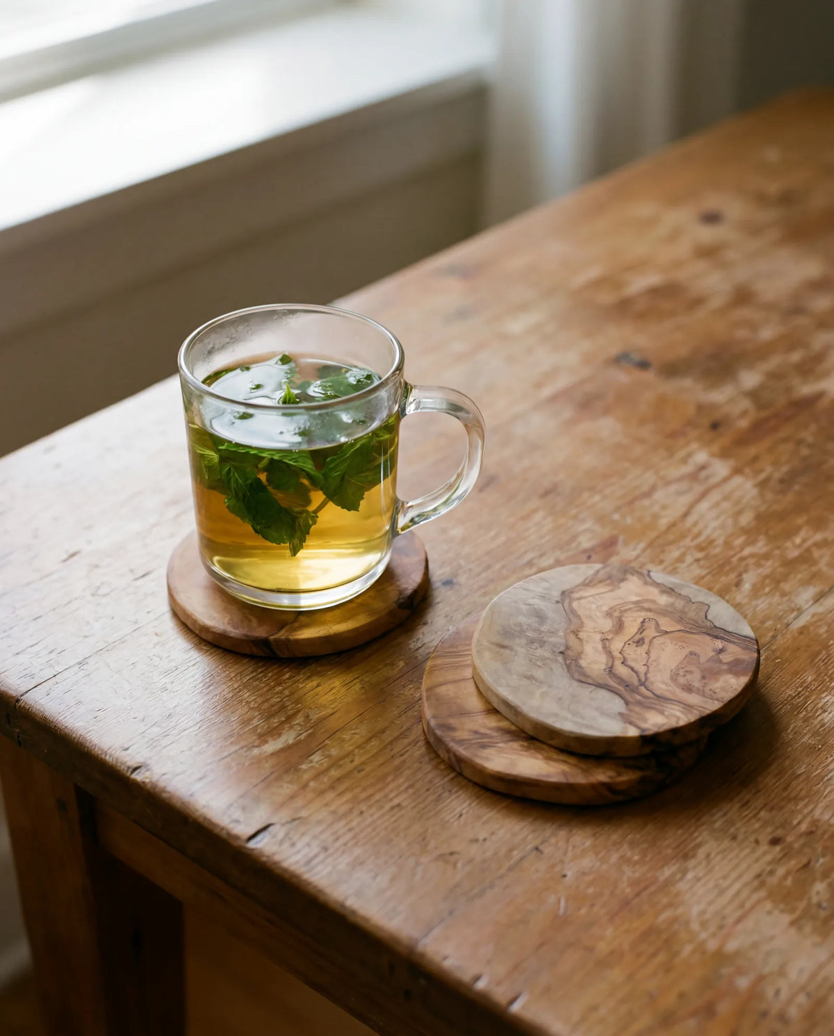 Glas Minztee auf rundem Olivenholz-Untersetzer auf einem Holztisch