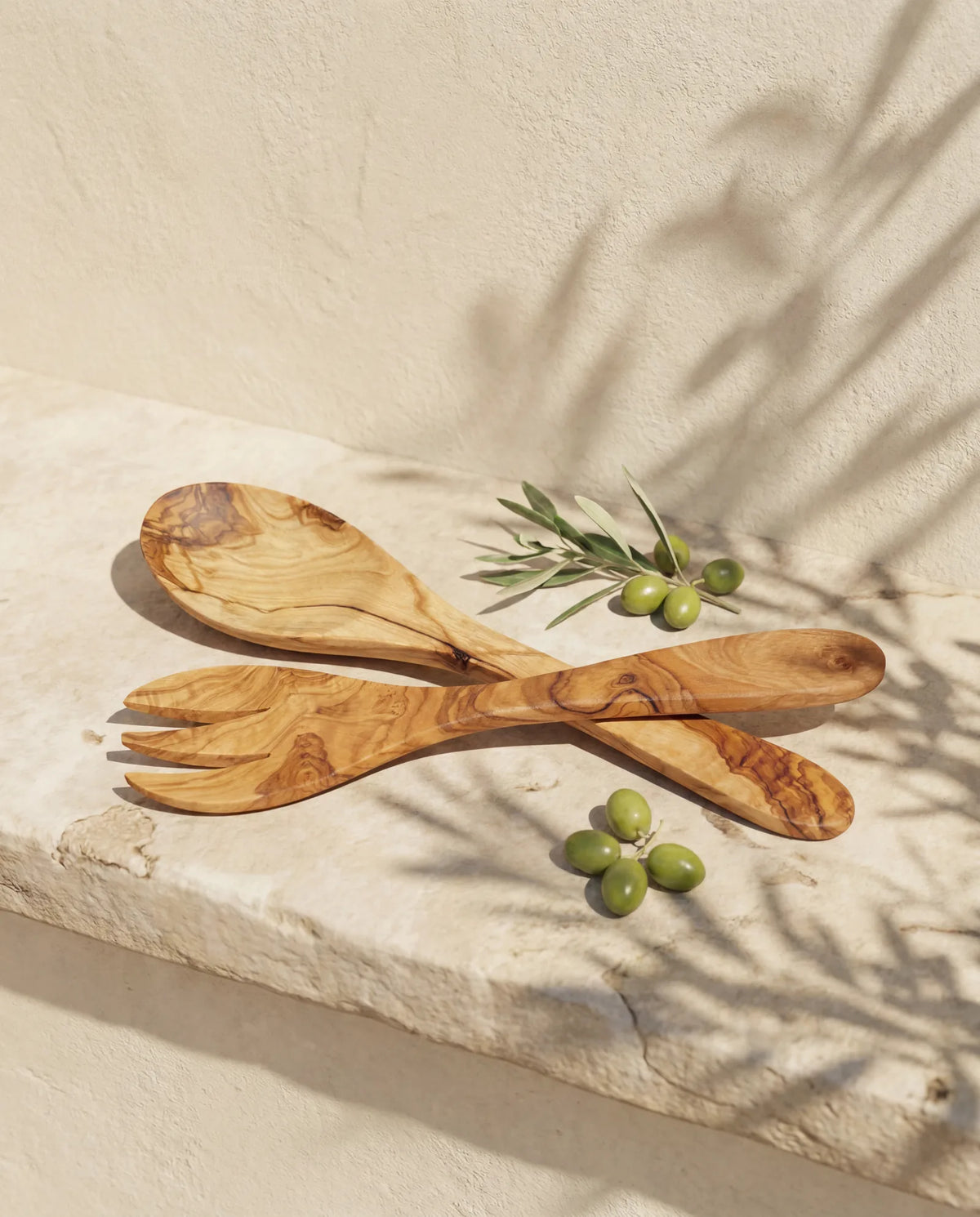 Salatbesteck aus Olivenholz, Löffel und Gabel gekreuzt an heller Wand
