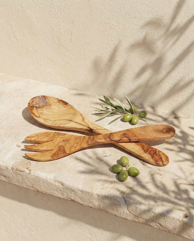 Salatbesteck aus Olivenholz, Löffel und Gabel gekreuzt an heller Wand