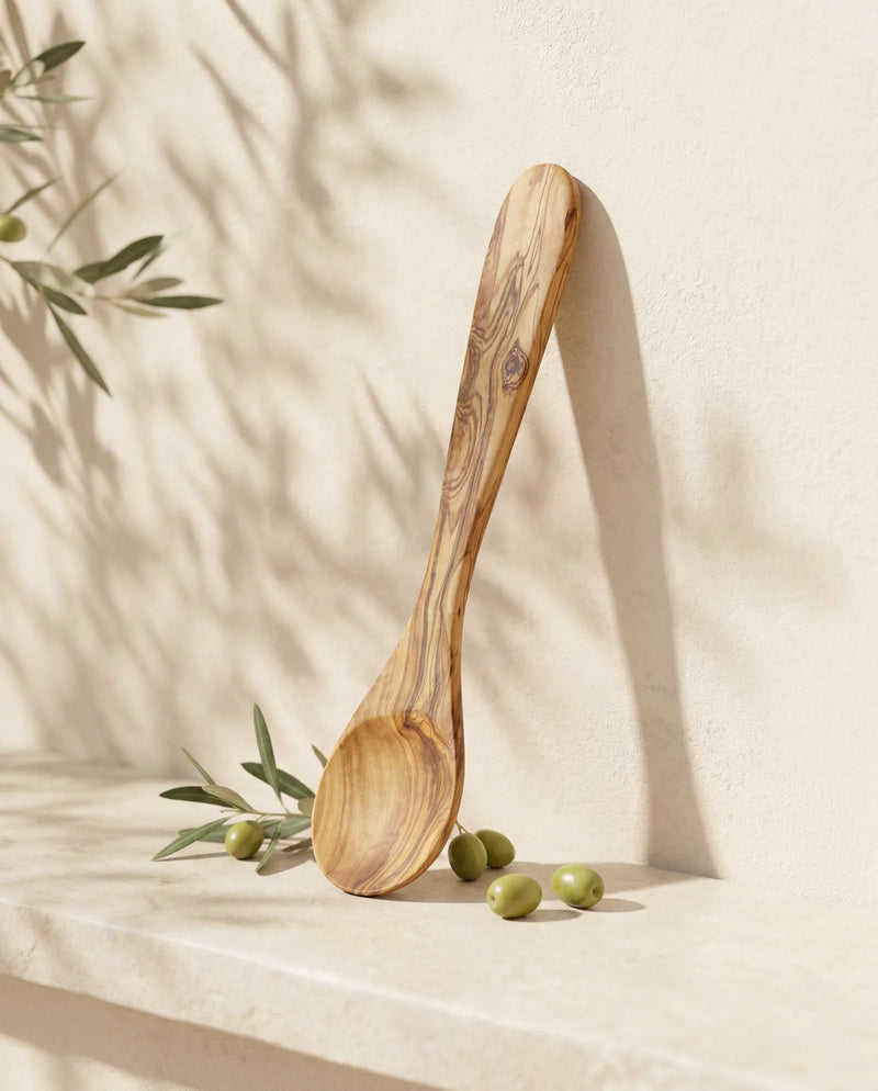 Servierlöffel aus Olivenholz an heller Wand, mit ovaler Laffe