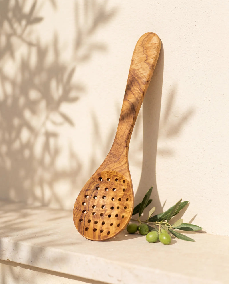 Siebkelle aus Olivenholz an heller Wand, mit gelochter Kelle